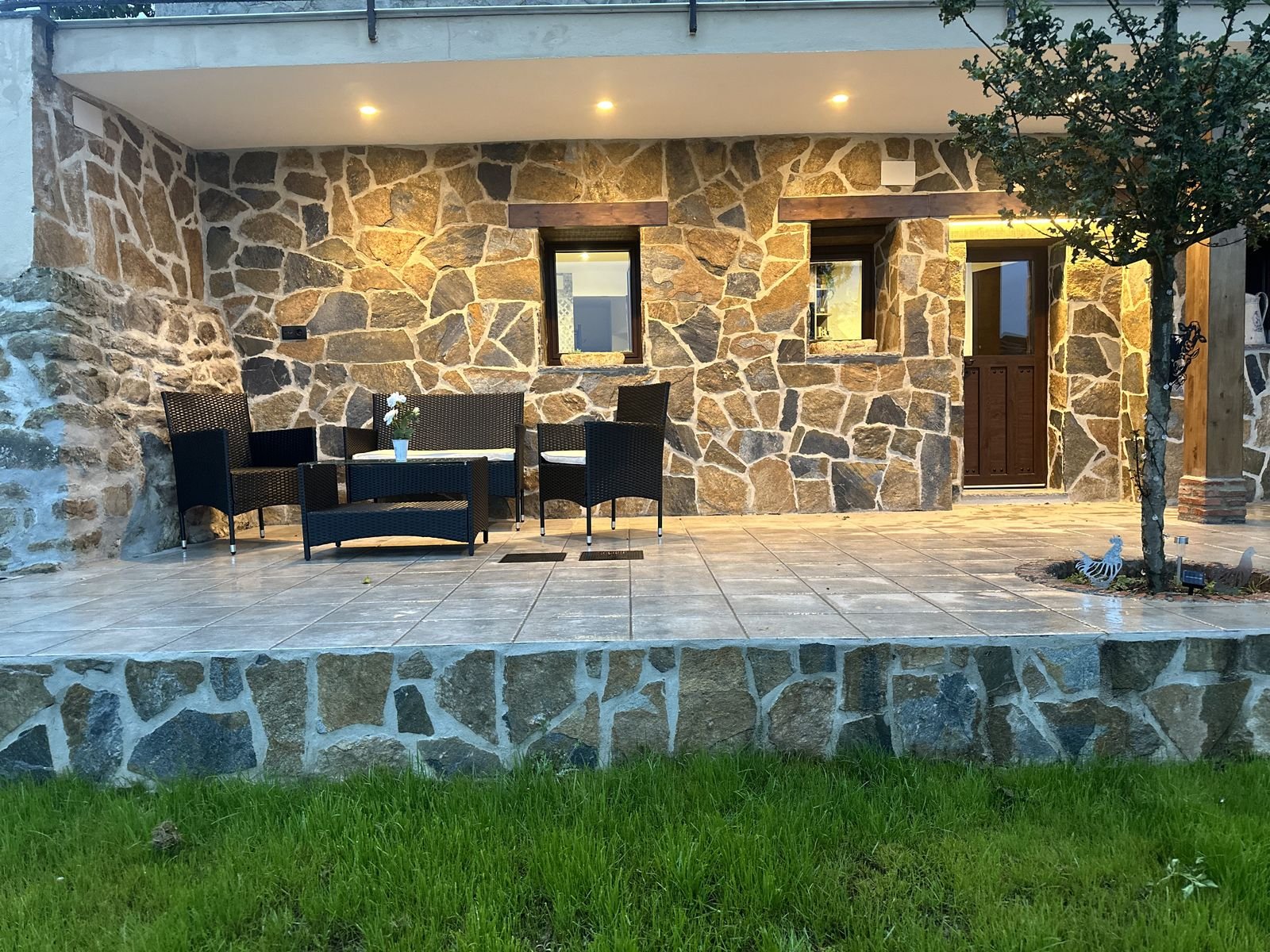 Stone porch lit up at dusk, with armchairs and a table
