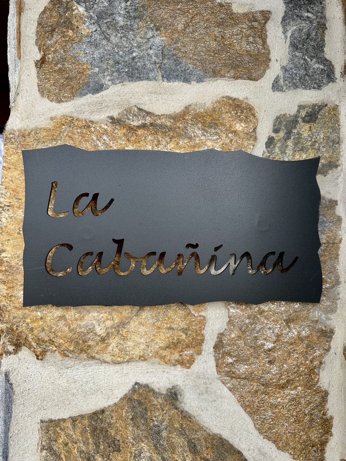 Iron sign for La Cabañina on the stone wall